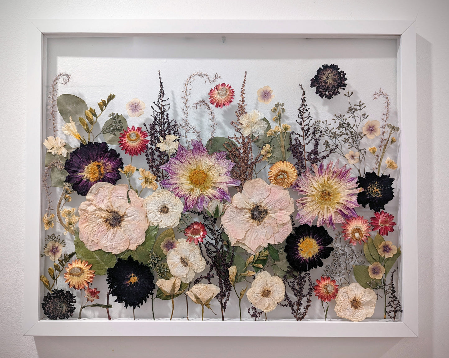 Unique art piece combining various pressed flowers and herbs in an abstract design.